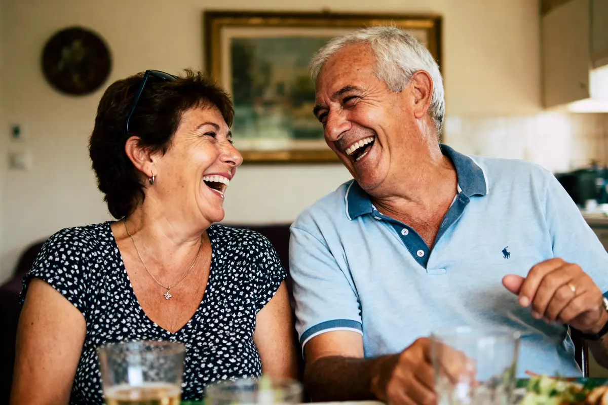 Un couple souriant et riant ensemble à une table, ambiance décontractée et chaleureuse.