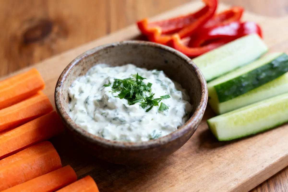 pexels-michal-pech-213601-757318 (1) Bol de sauce blanche avec persil, entouré de bâtonnets de carottes, poivrons rouges et concombres, sur planche bois.