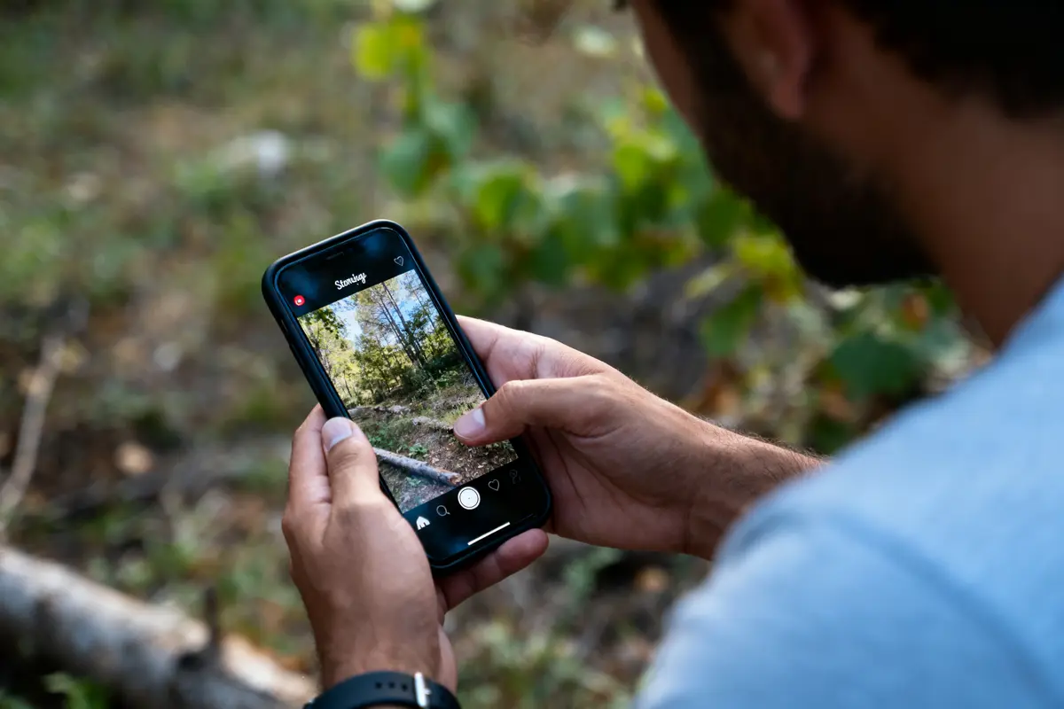 pexels-michal-pech-213601-757318 (1) Personne utilisant un smartphone pour photographier une forĂŞt en plein air, avec l'application d'appareil photo ouverte.