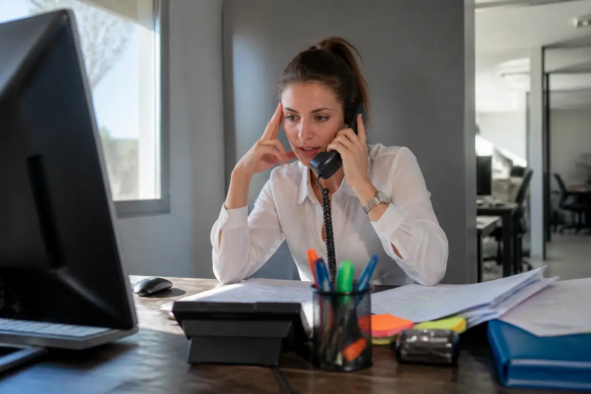 pexels-michal-pech-213601-757318 (1) Jeune femme au bureau, parlant au téléphone, entourée de papiers et de fournitures de bureau colorées.