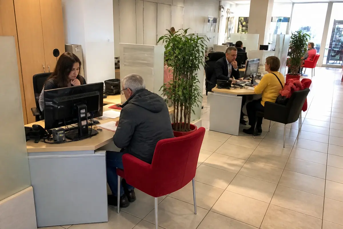 Des personnes discutent avec des conseillers dans un bureau moderne. Ordinateurs, chaises rouges et plantes vertes.